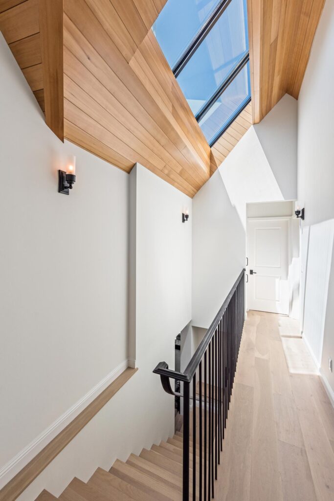 Second story landing with white oak floors in light filled stairwell with skylight and hemlock wood ceiling